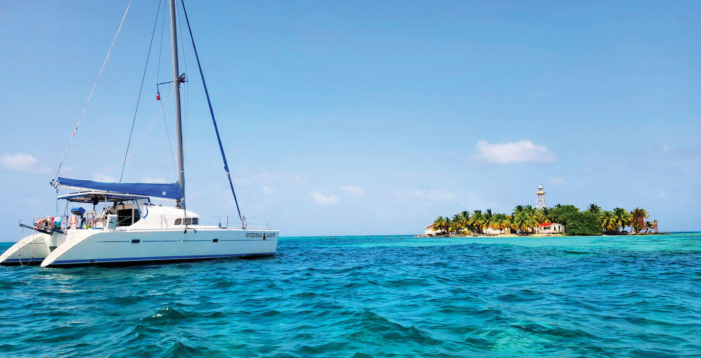 Catamaran sail boat sailing towards a lush palm tree covered island in Belize
